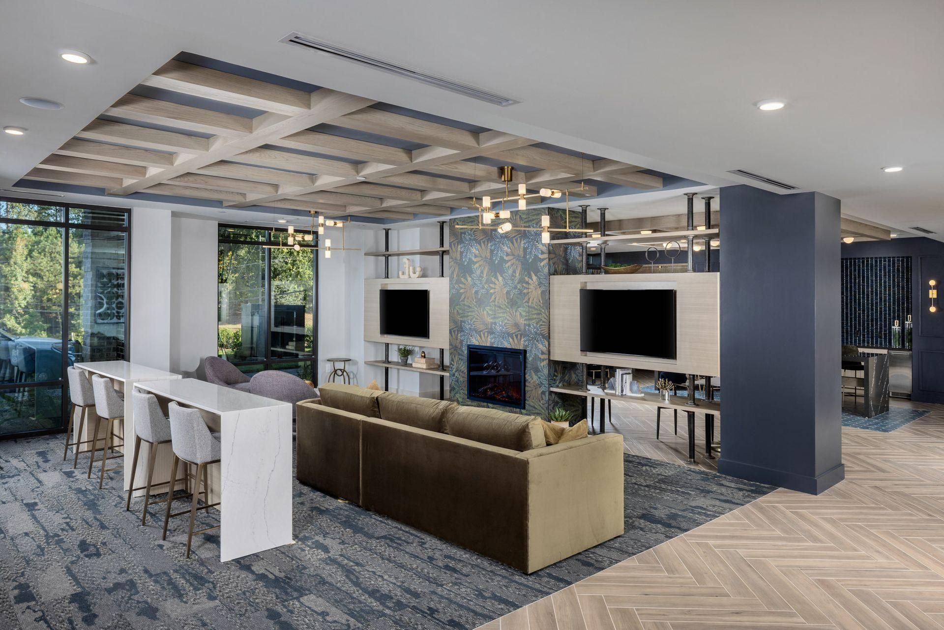 Modern open office lounge with desks, monitors, white bar counter, sofa, and patterned blue carpet.