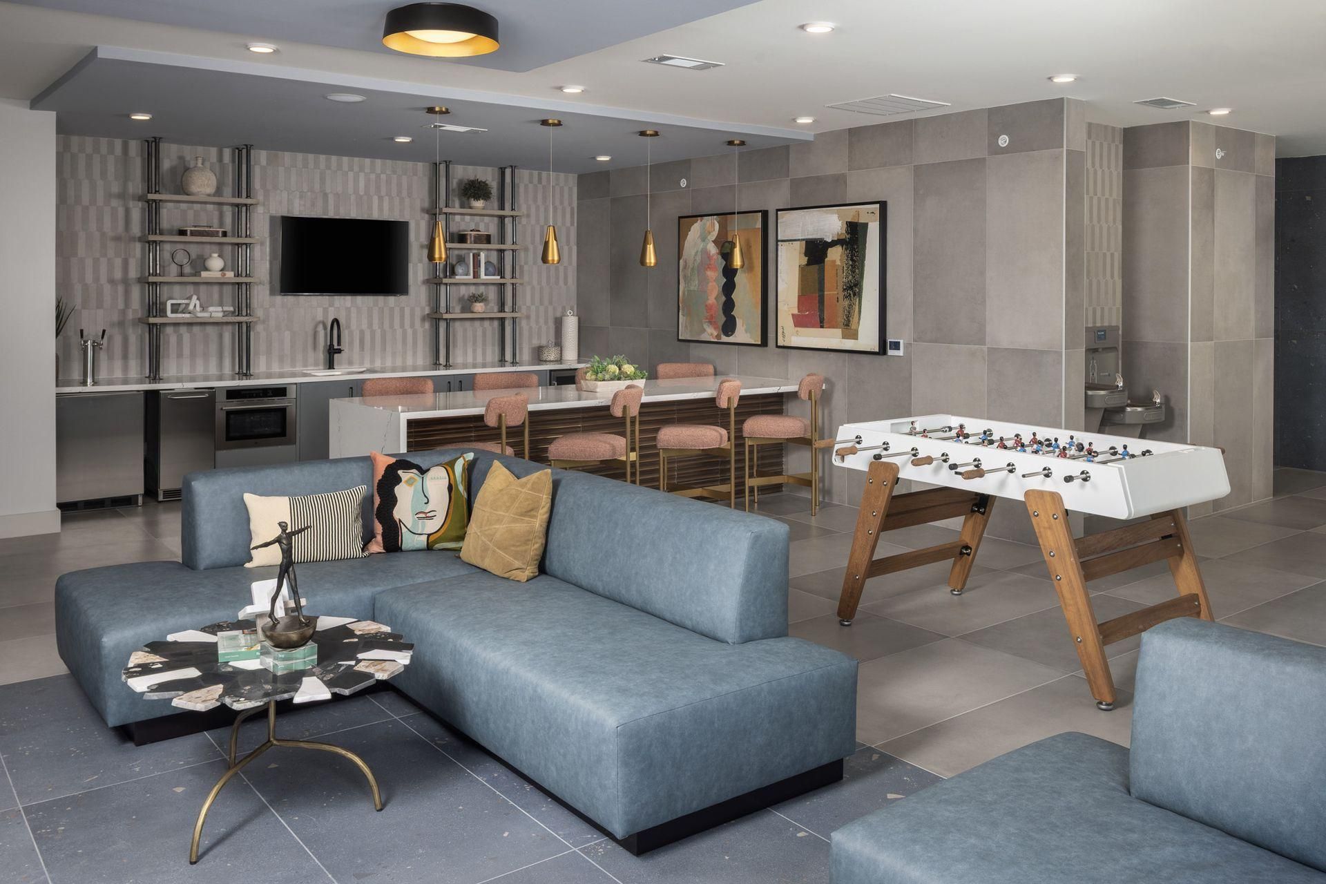 Modern open-plan living room with gray sofa, dining table, wall TV, and foosball table