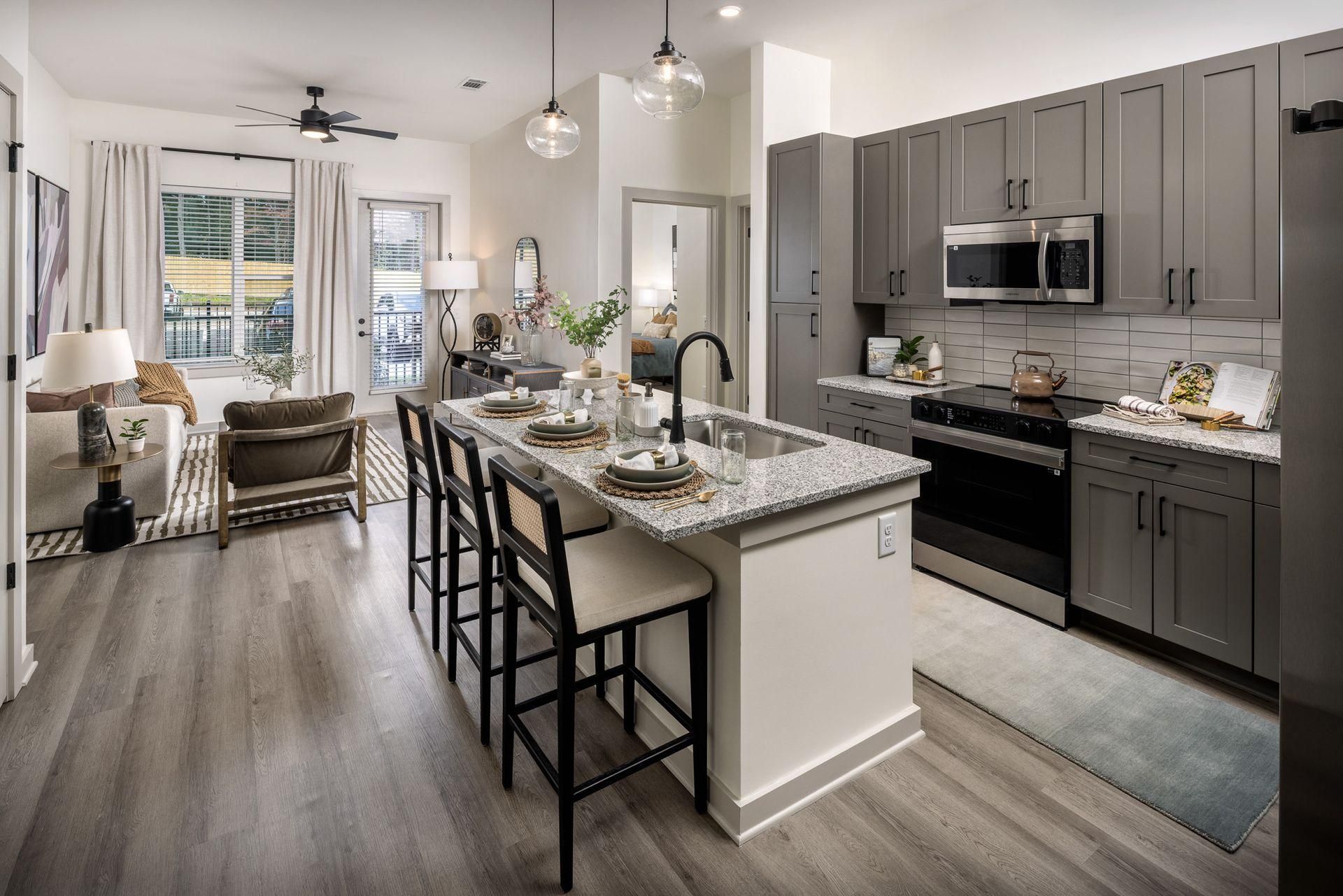 Modern kitchen and living area with gray cabinets, island seating, and large windows looking outside