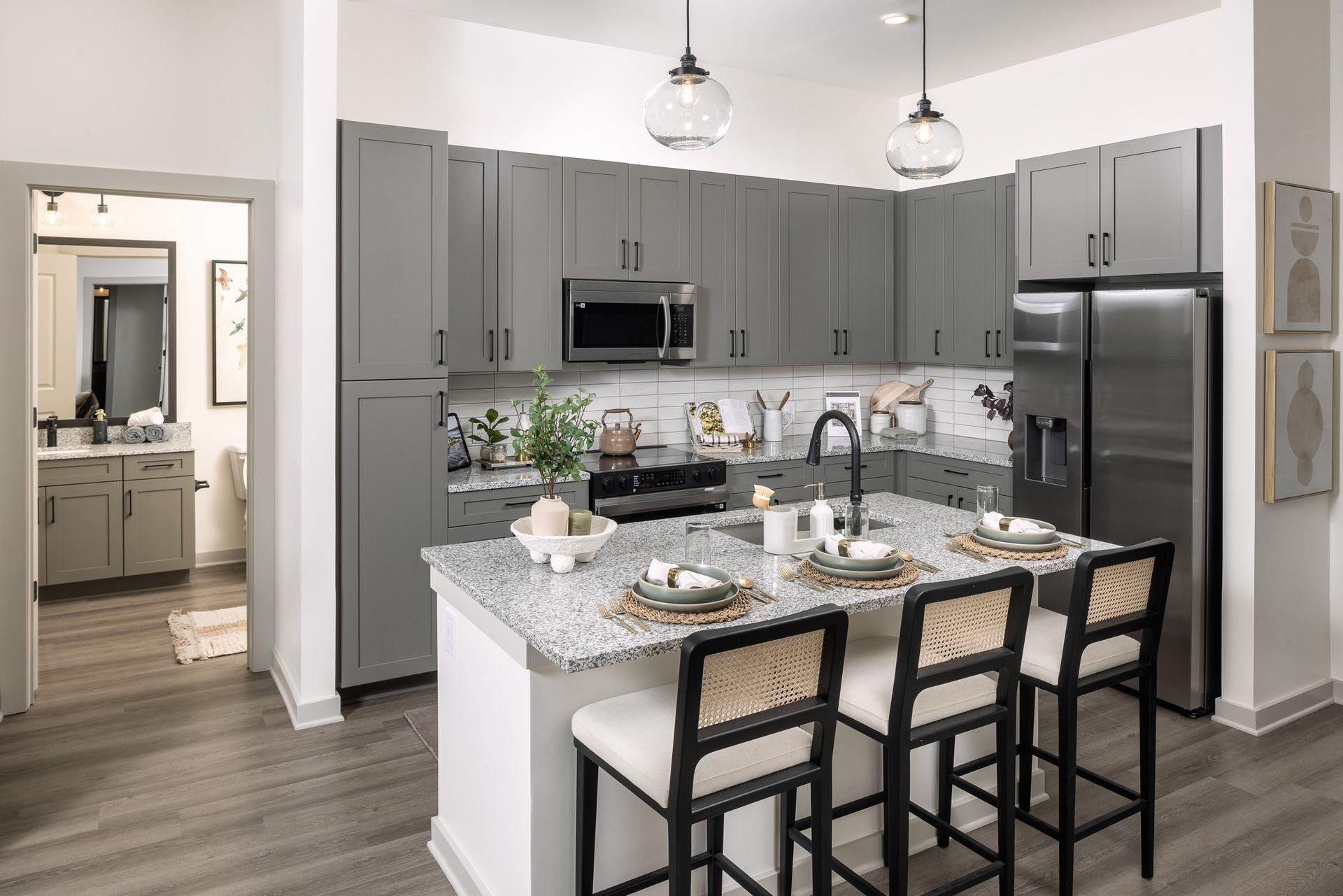 Modern kitchen with gray cabinets, island seating, stainless appliances, and pendant lights