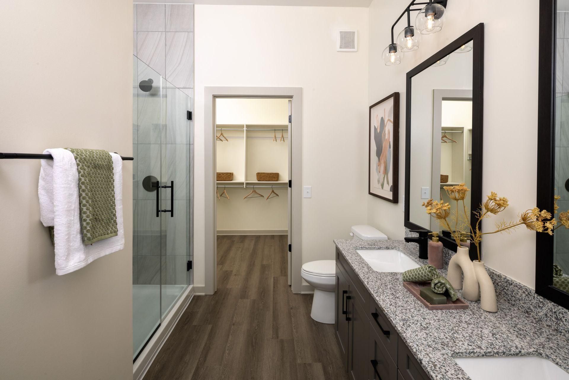 Modern bathroom with glass shower, double vanity, mirrors, and white towels on a gray and black patterned counter