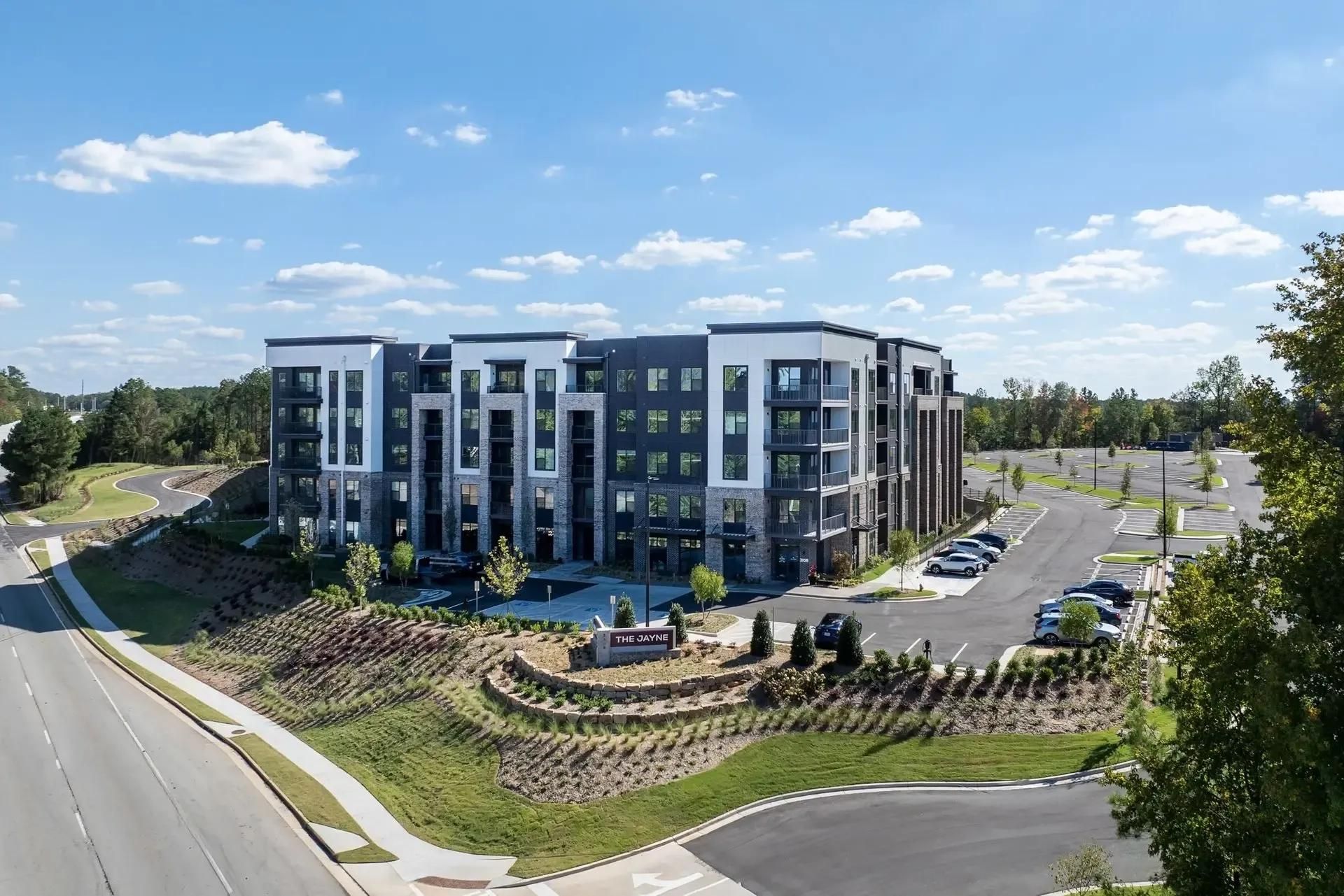 Modern apartment complex with parking lot and landscaped grounds under a blue sky