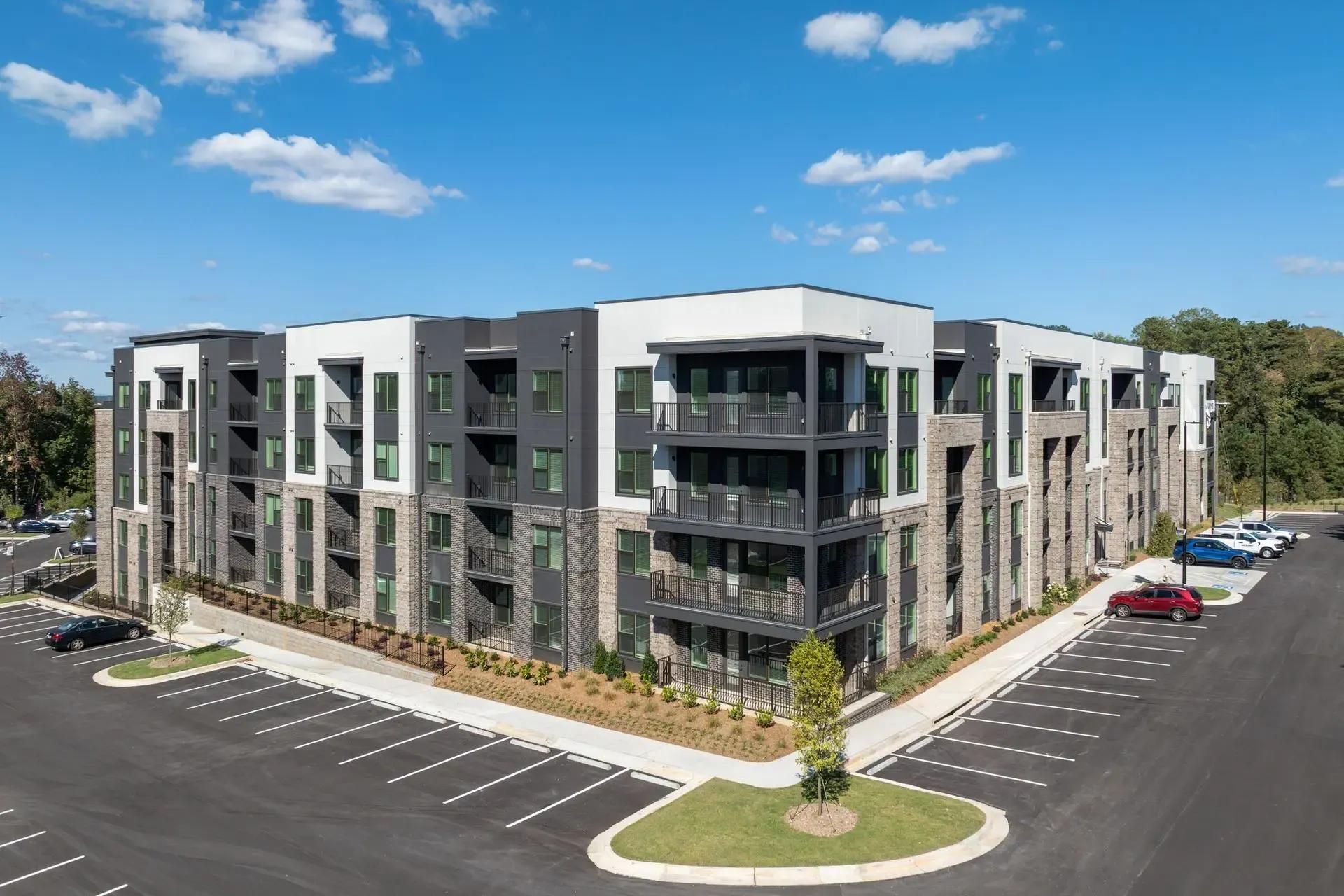 Modern gray apartment building with balconies beside a parking lot under a blue sky