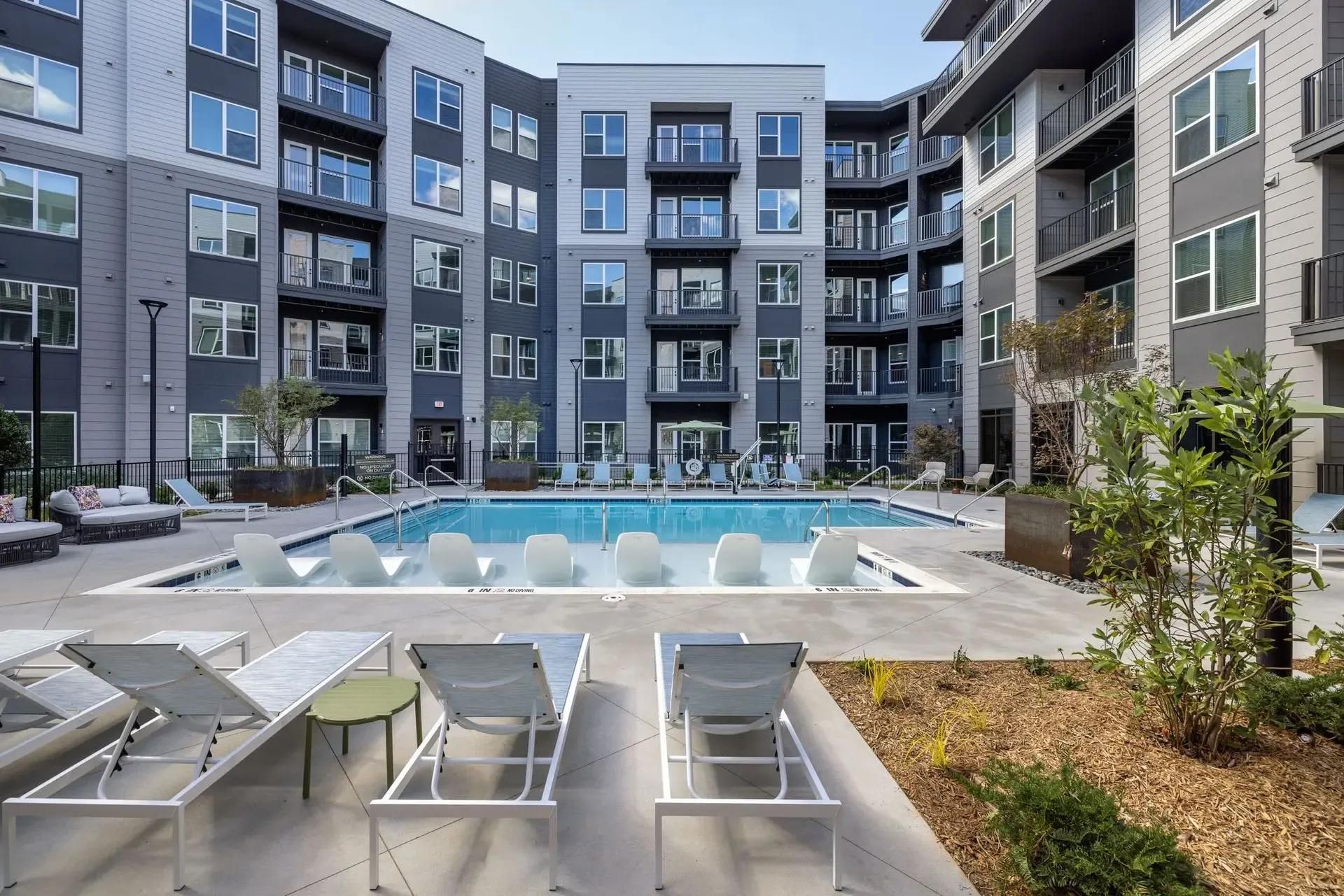 Modern apartment courtyard with lounge chairs and a central fountain surrounded by gray buildings