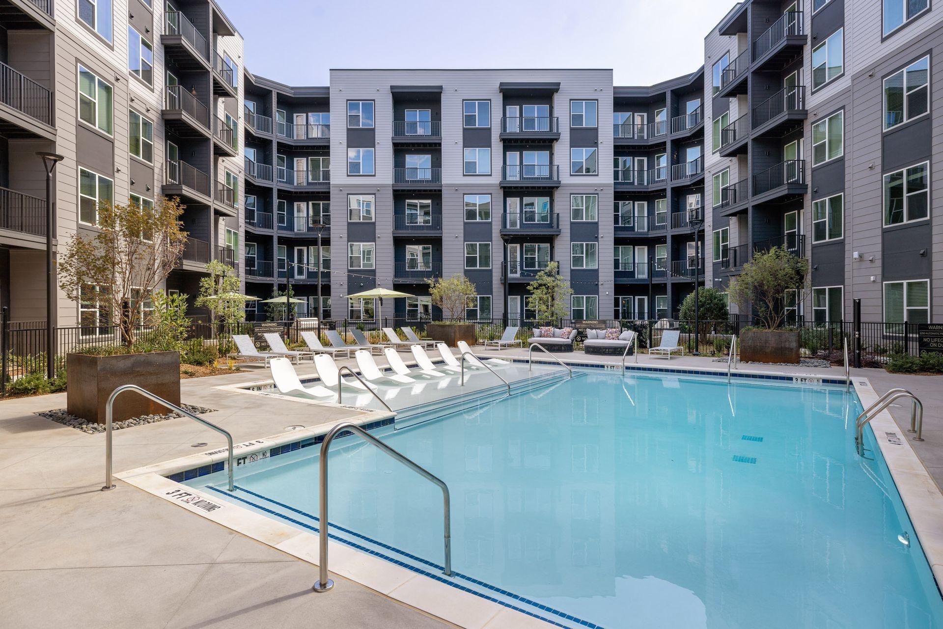 Modern apartment courtyard with a swimming pool, lounge chairs, and surrounding buildings