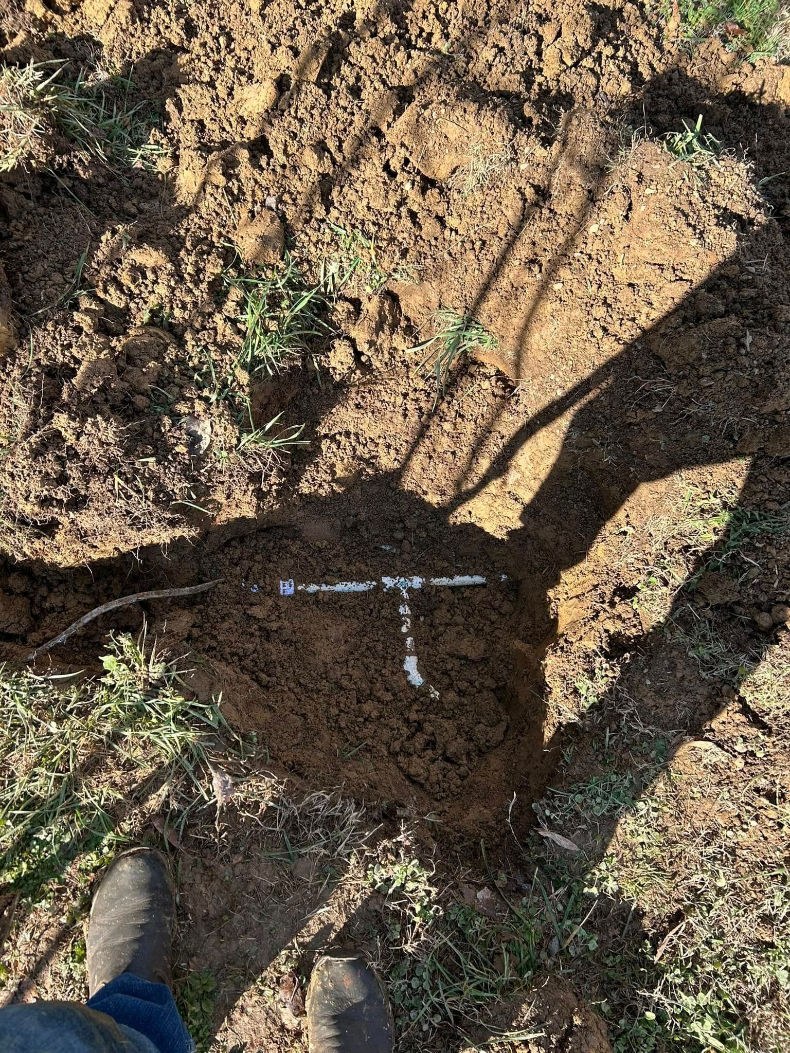 A white T-shape marked with spray paint on dry, churned earth, seen from a high angle with a shadow cast across the ground.
