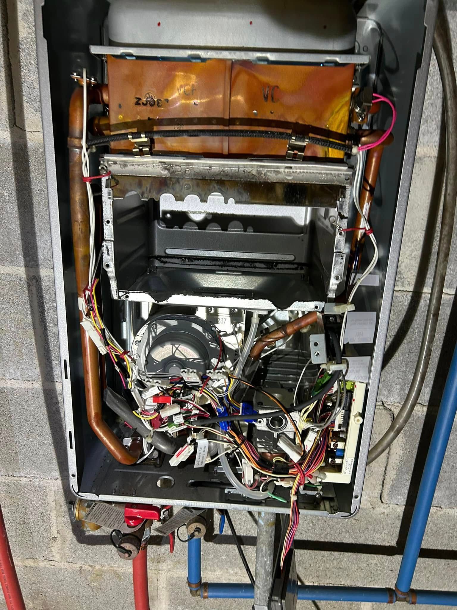 Interior view of a wall-mounted tankless water heater with its metal casing removed, showing internal wiring and pipes.