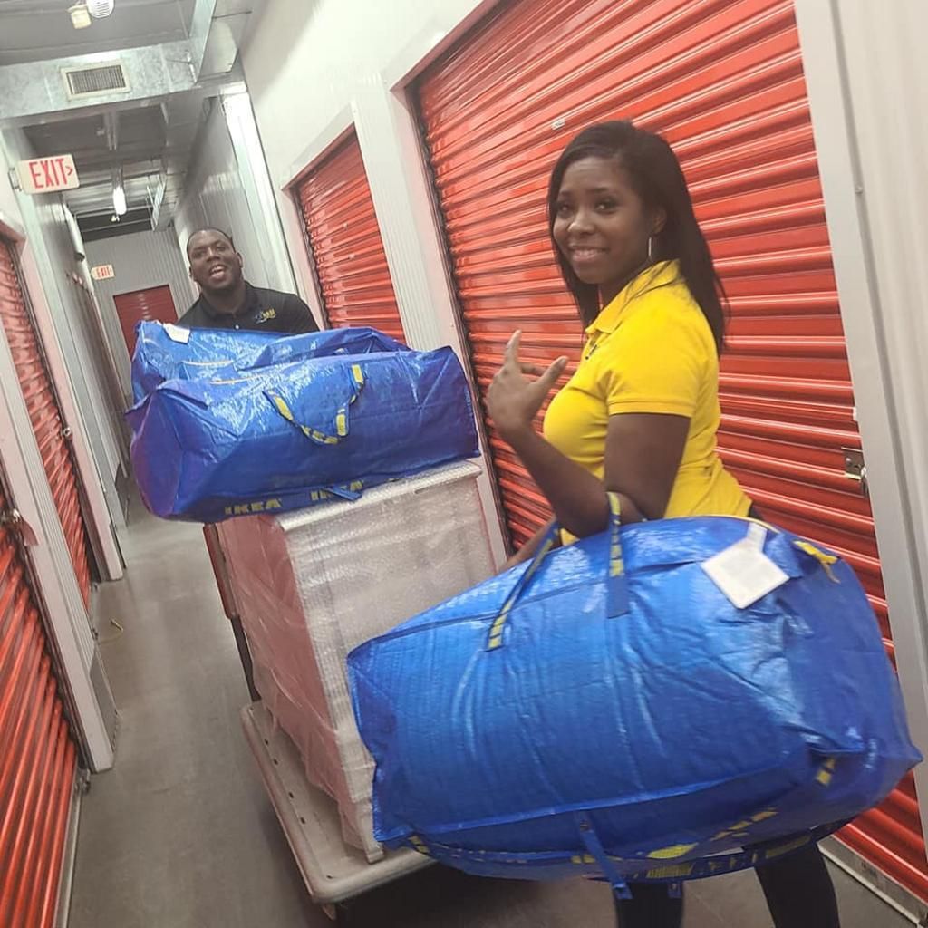 Woman with blue bag and man with cart in storage unit hallway. Red doors.