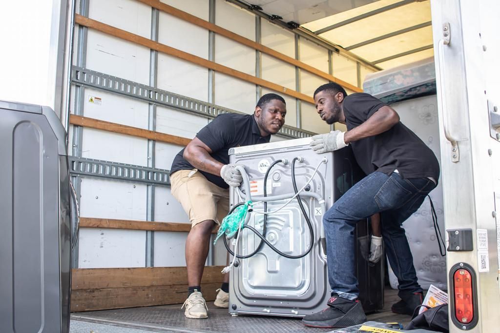 Two people load a silver appliance into a truck.