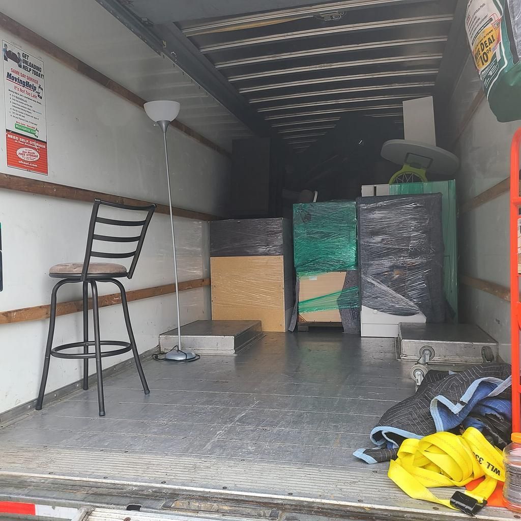 Inside a moving truck loaded with furniture, including a chair, lamps, and wrapped items.