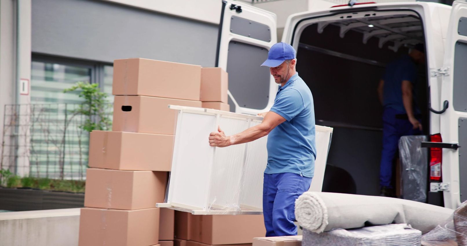 Movers loading a white cabinet into a van filled with boxes and a rolled rug.