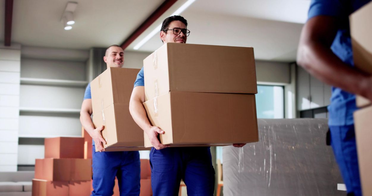 Movers loading a white cabinet into a van filled with boxes and a rolled rug.