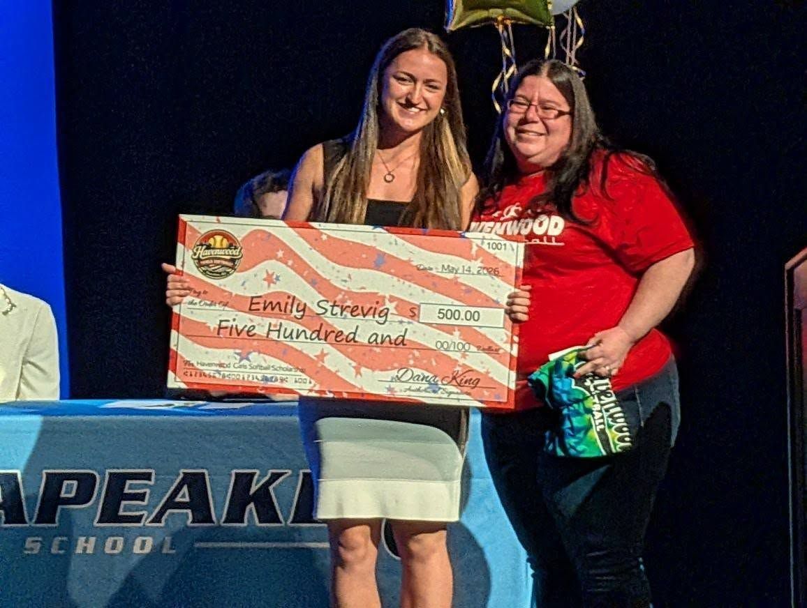 Two women onstage holding a large award check, smiling in front of a blue backdrop.