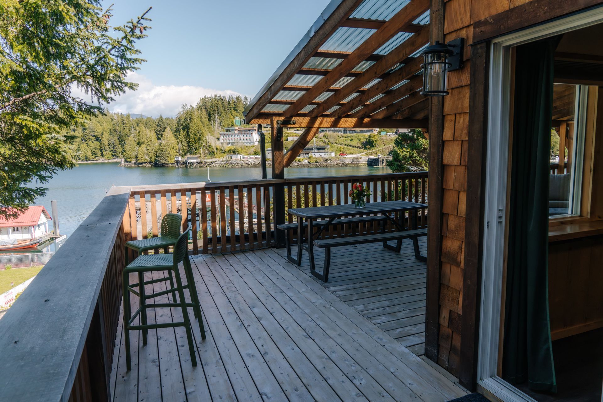 Wooden deck with a picnic table and bar stools overlooking a scenic lake surrounded by trees and mountains.