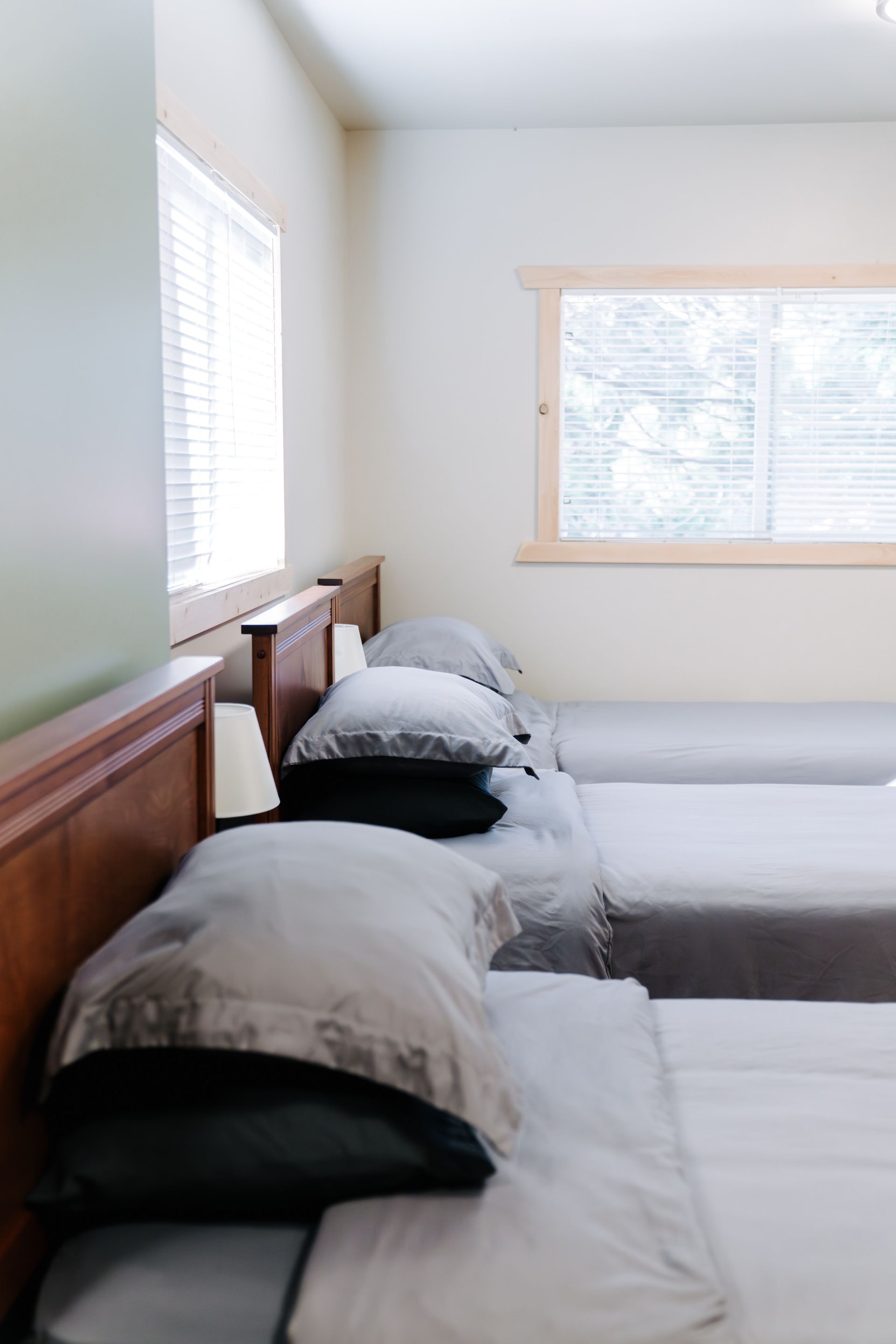 A bedroom with two neatly made twin beds, each featuring grey sheets, black bottom pillows, and light grey top pillows.