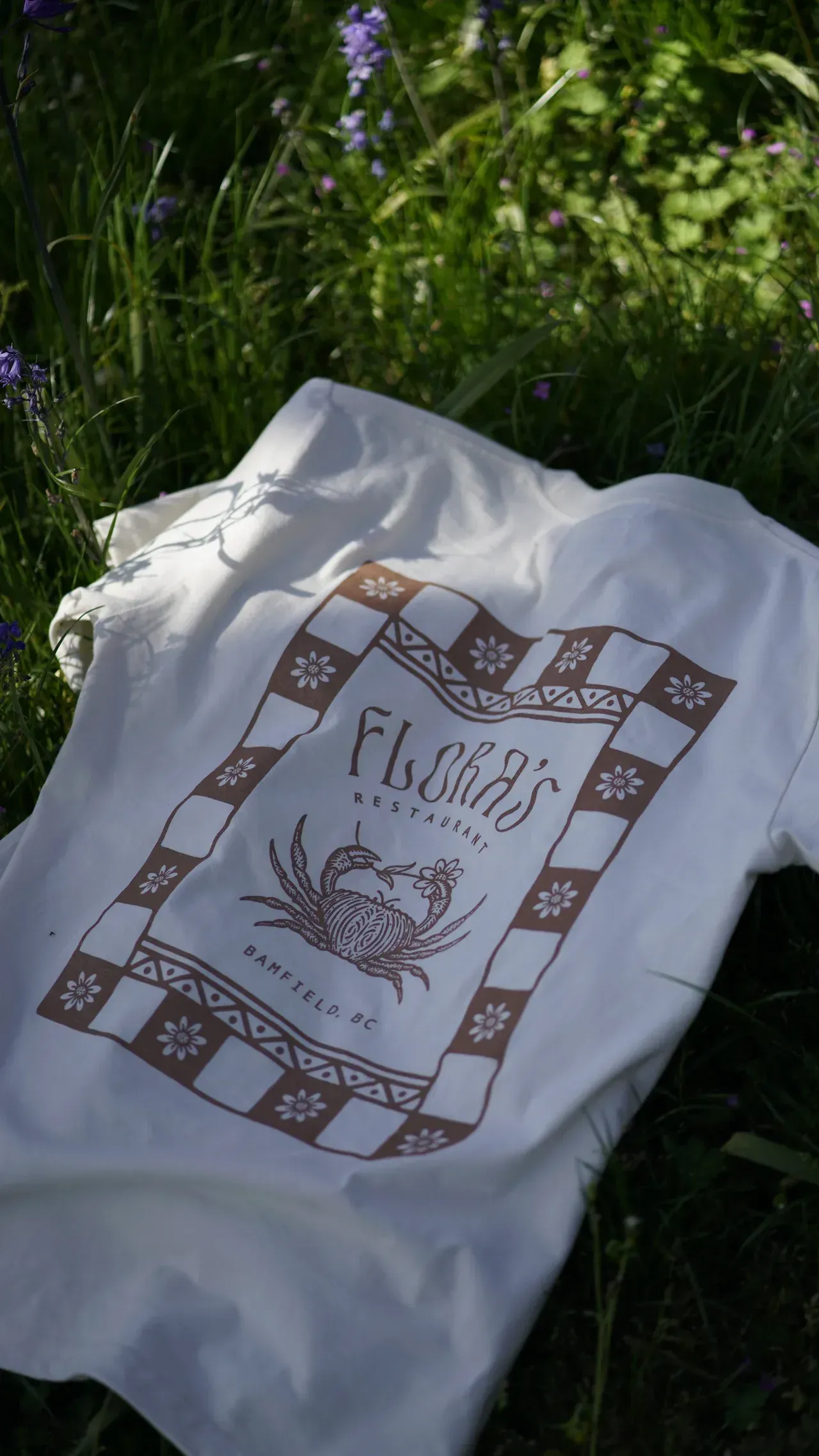 A white t-shirt with a checkered pattern is laying in the grass.