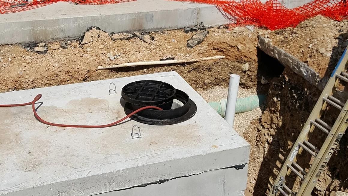 Concrete utility box with coiled black cable and white pipe at a construction site