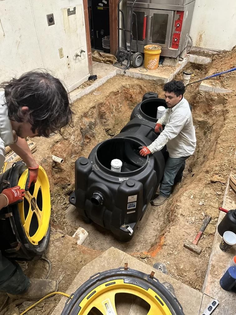 Workers installing a black septic tank in a trench at a construction site, with yellow lids nearby.