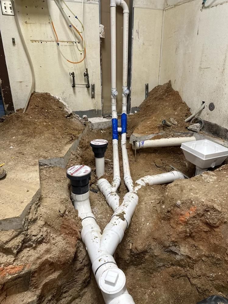 Plumbing pipes and drains installed in an unfinished basement with exposed dirt and concrete walls