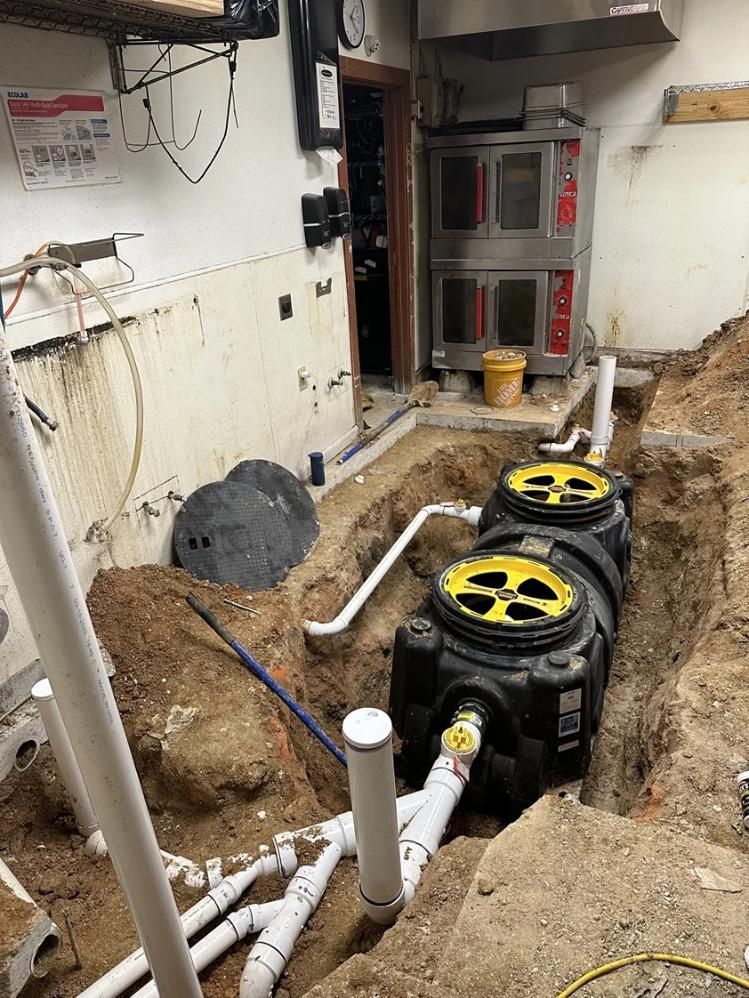 Utility basement with a trench, white pipes, and black ventilation fans installed in the floor