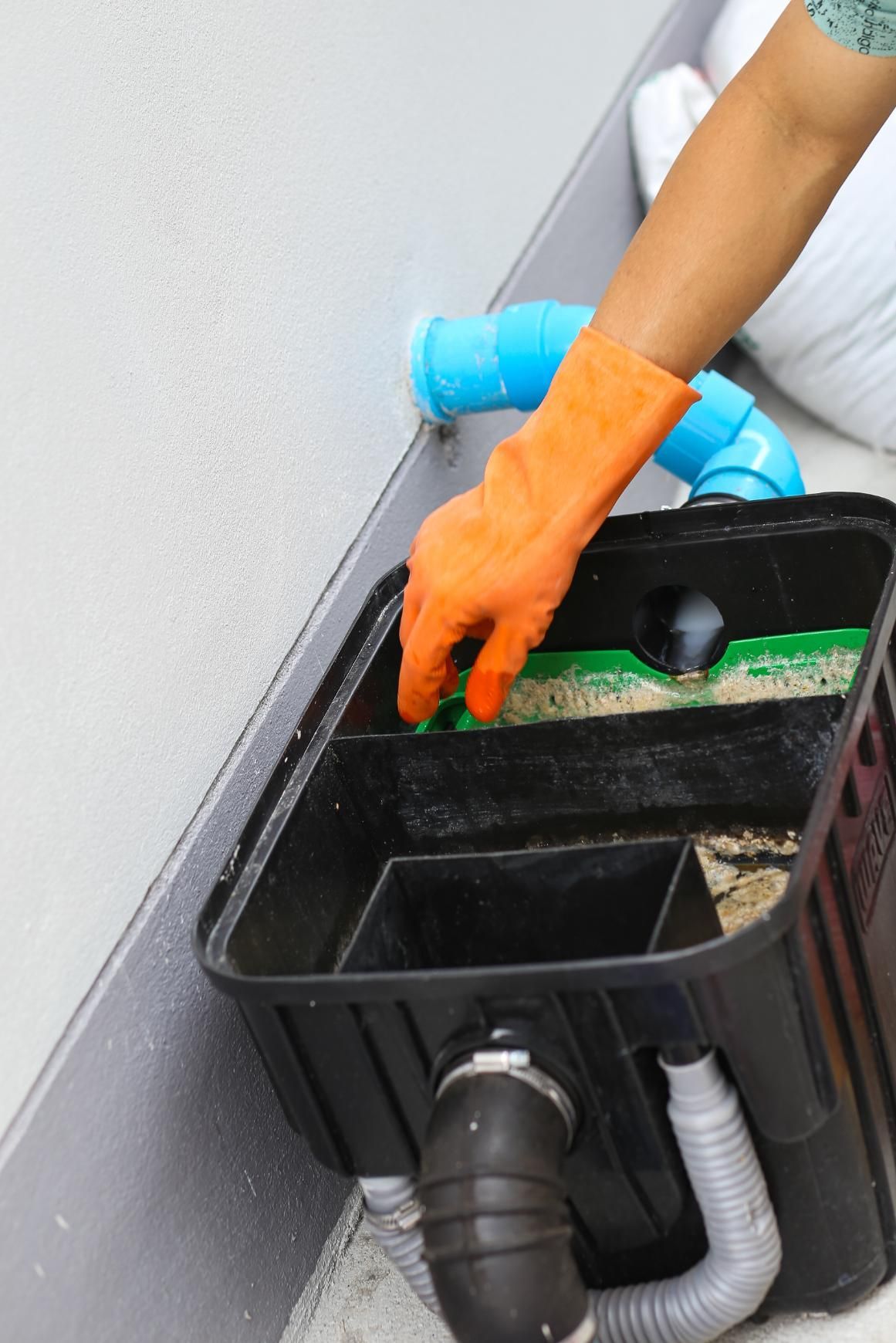 Gloved hand cleaning a black filter box with a brush and hose near a wall
