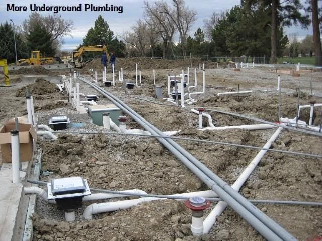Underground plumbing site with exposed white pipes and utility boxes in a muddy construction area
