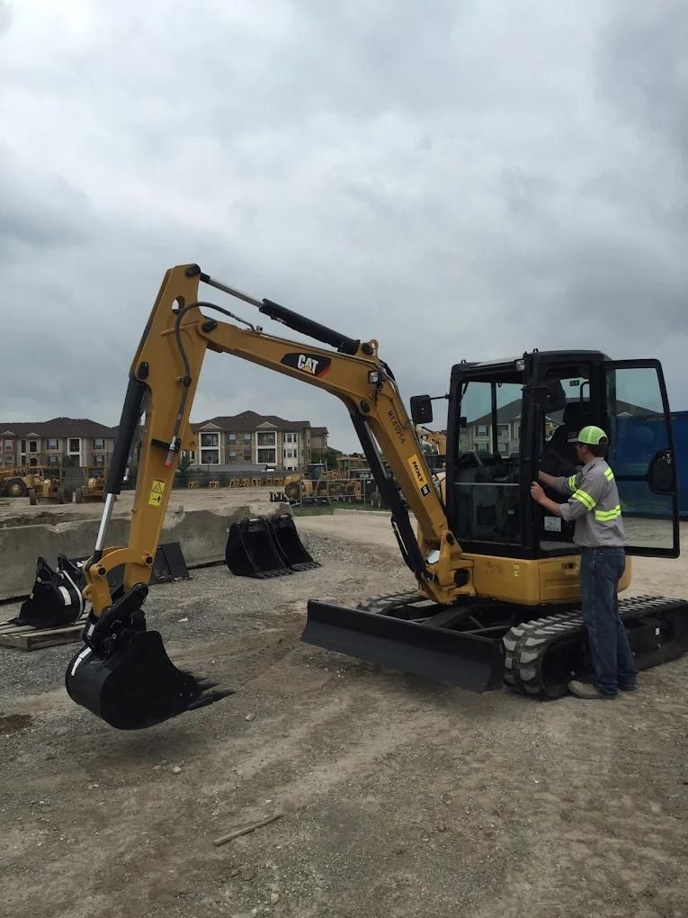 Construction worker beside yellow excavator on a gravel site under a cloudy sky