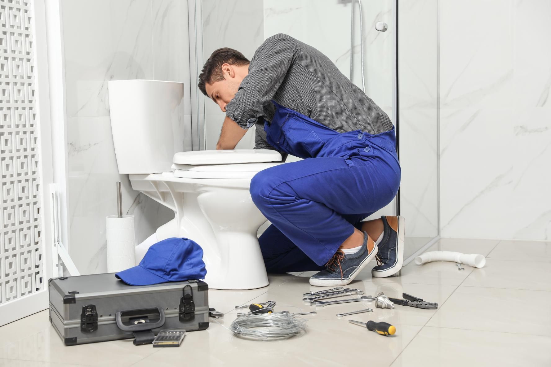 Plumber repairing a toilet in a bathroom, with tools and parts scattered on the floor.