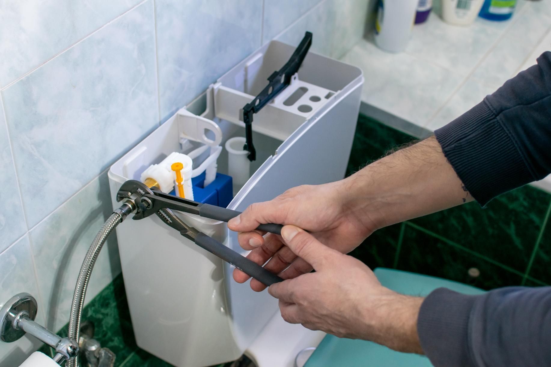 Hands adjusting a sink faucet hose beside a bathroom fixture and cleaning supplies