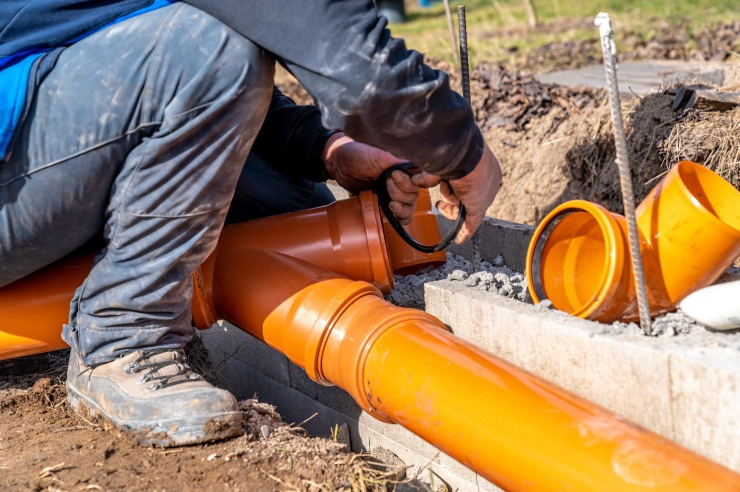 Worker installing orange sewer pipes in a trench with tools and concrete edges