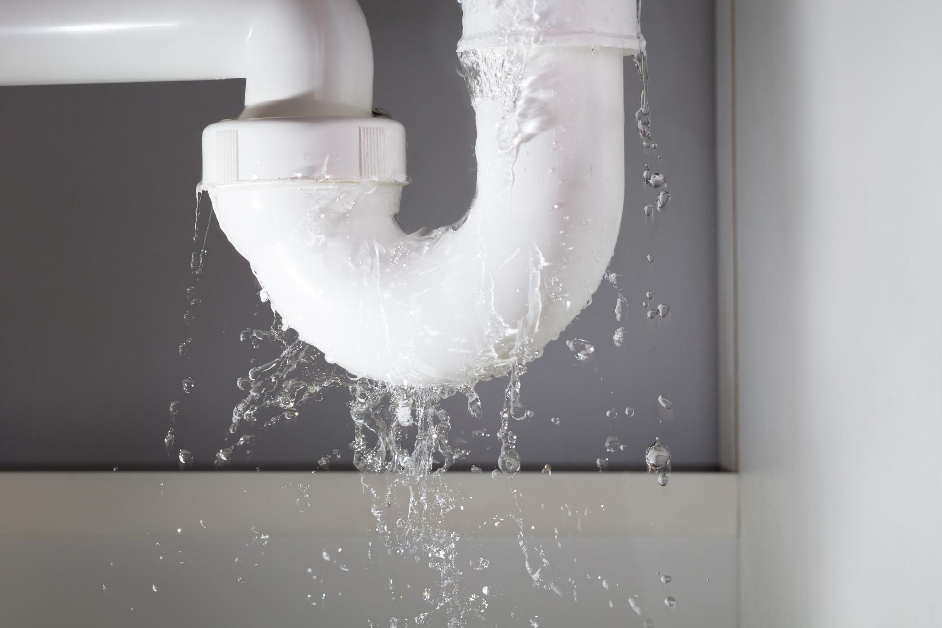 Leaking white sink drain pipe with water dripping into cabinet below