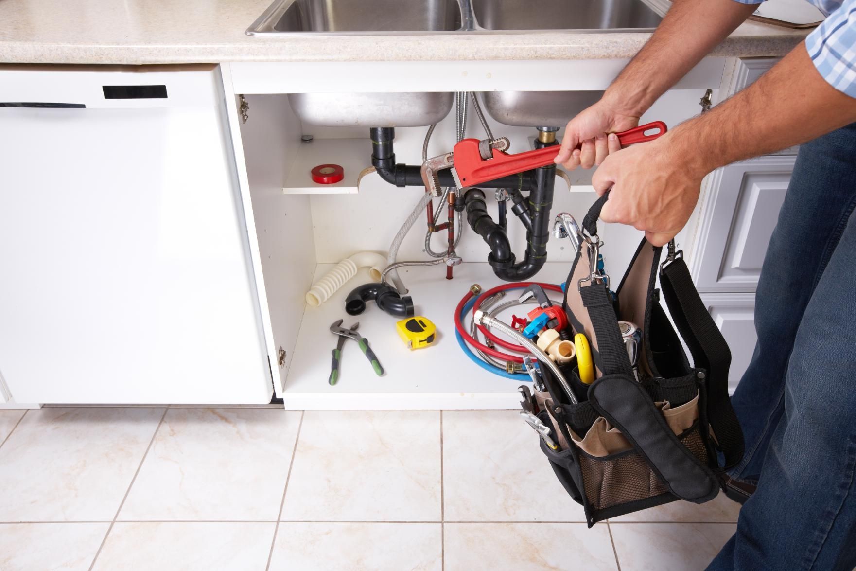 Plumber working under a kitchen sink with tools and exposed pipes on the floor