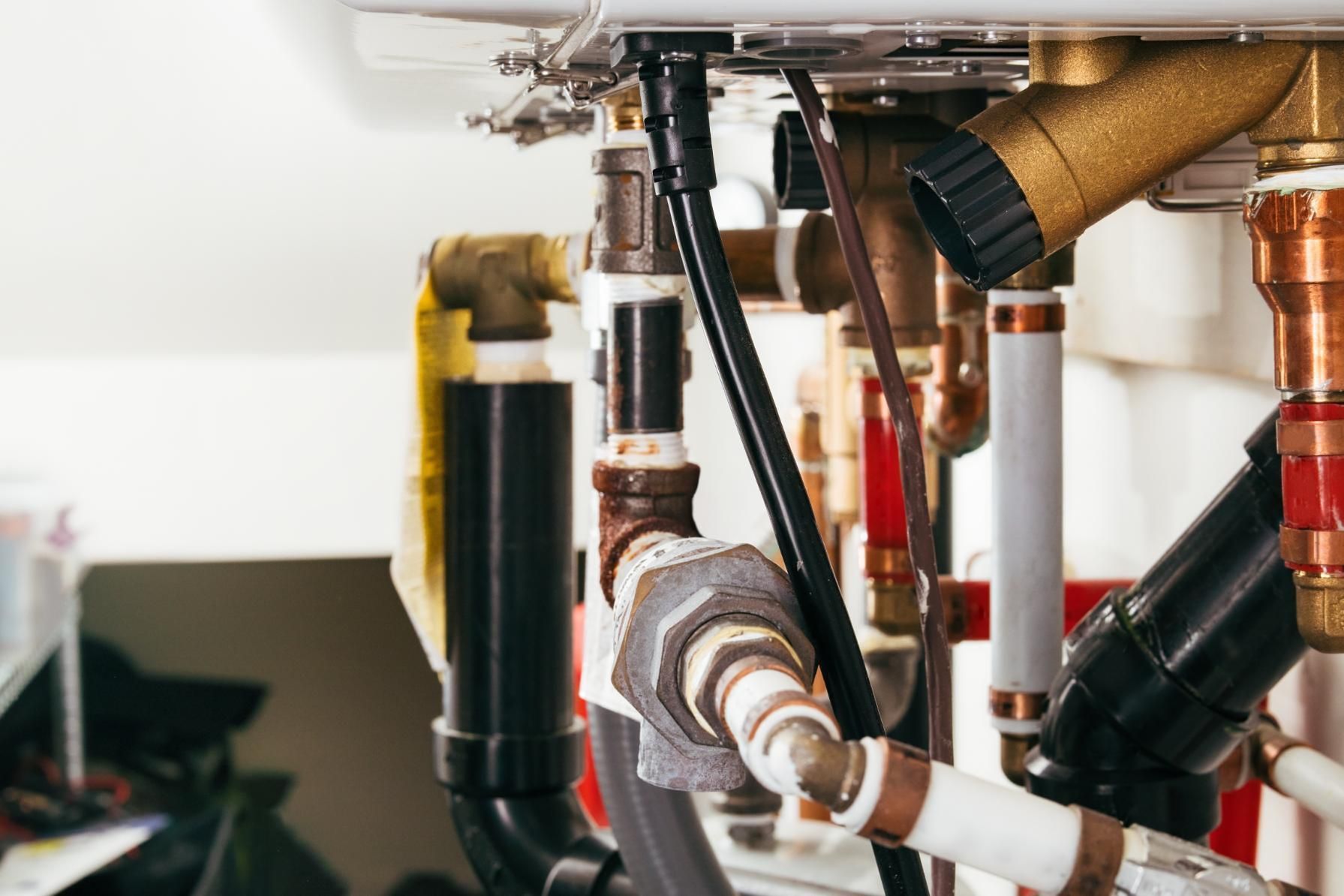 Close-up of exposed plumbing pipes and valves under a sink, with copper and black fittings.