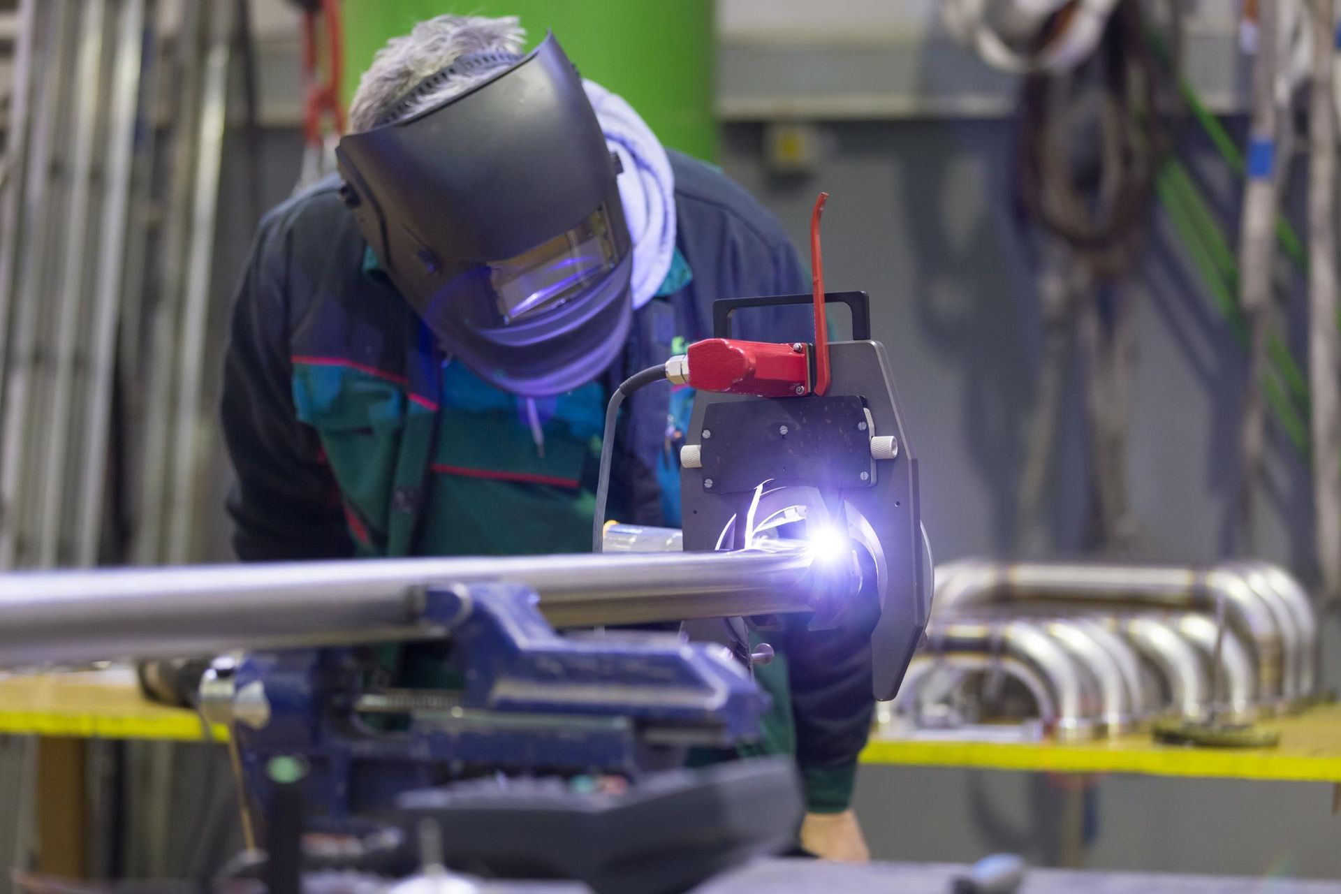 Welder in protective gear welding a metal pipe in an industrial workshop