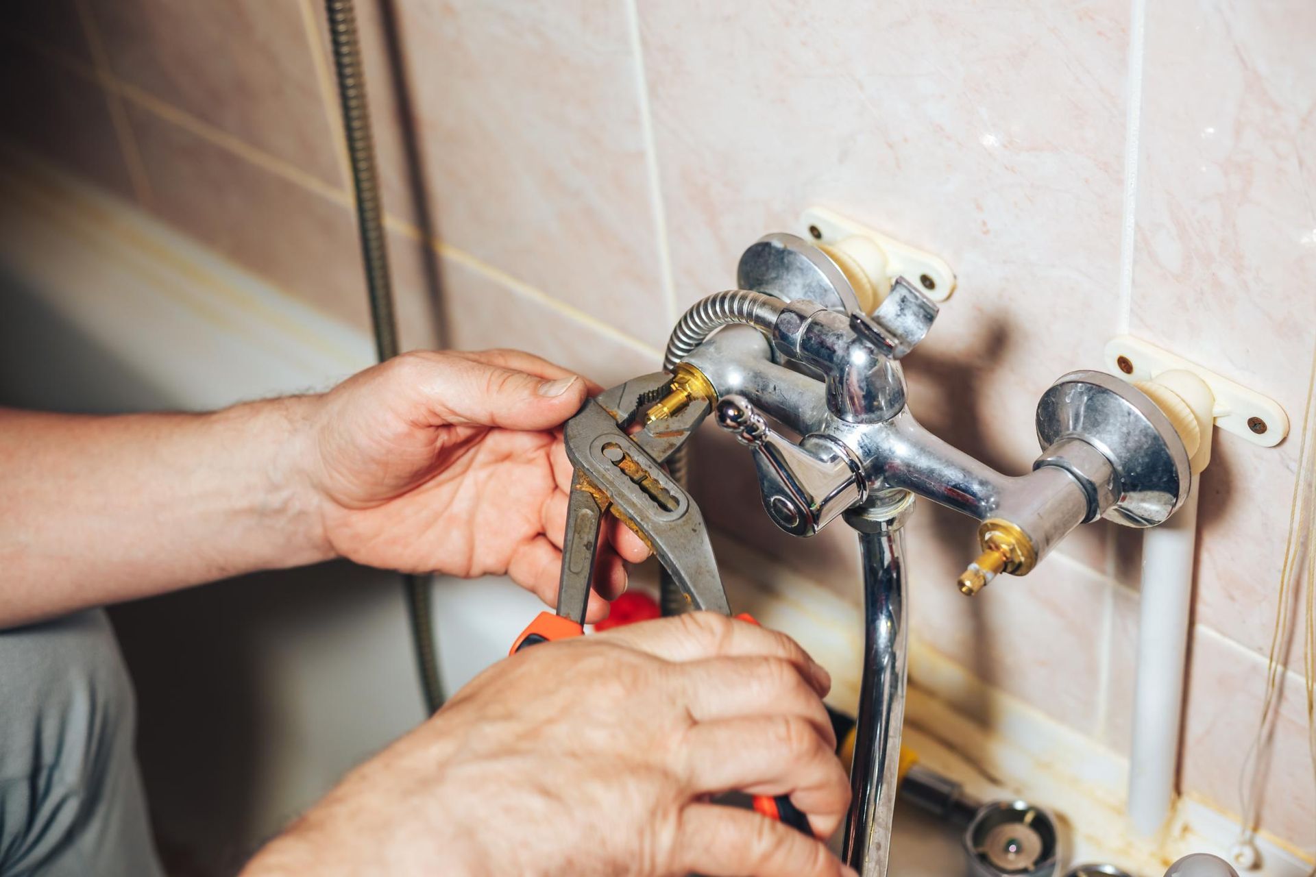 Hands adjusting a chrome faucet valve with a wrench on a tiled wall