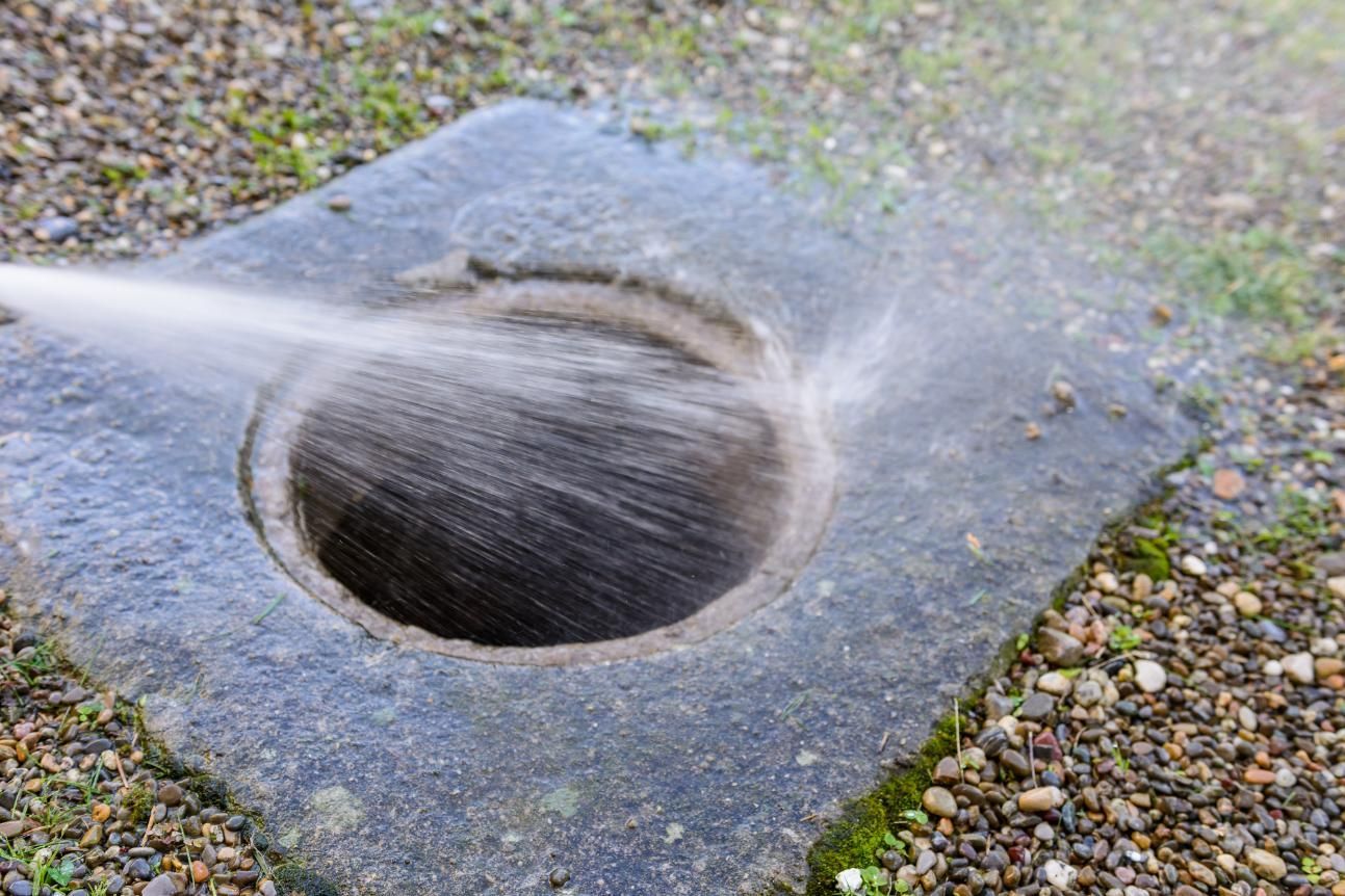 Water streaming into a round drain opening set in a wet gravel surface.