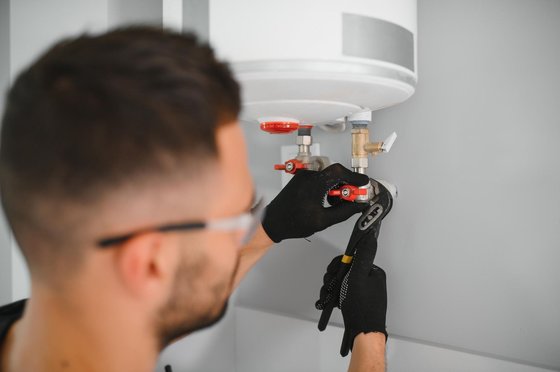 Technician using tools to service a white ceiling-mounted water heater.