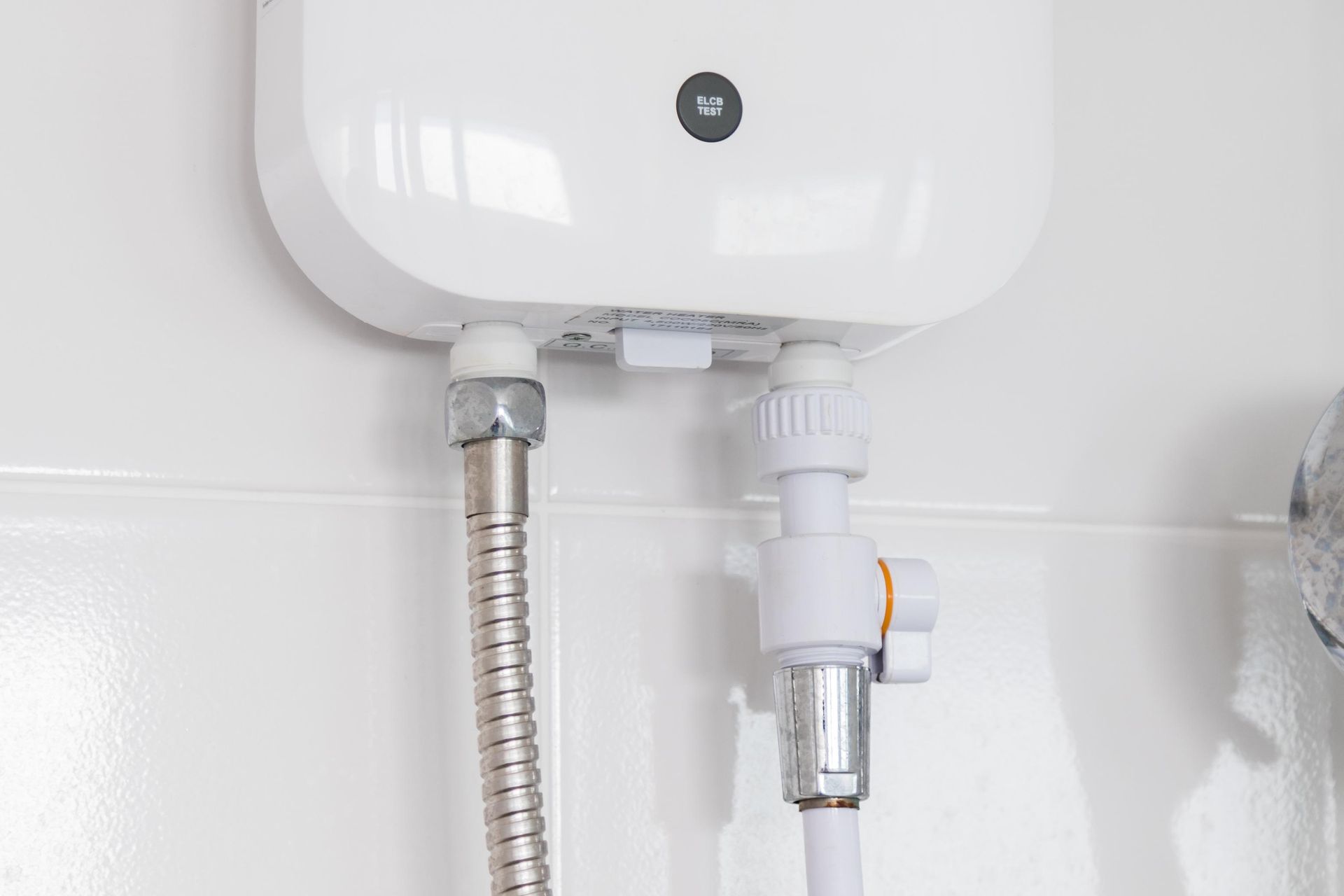 White wall-mounted water heater with metal hose and drain pipe against tiled wall