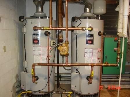 Two white water heaters with copper piping and valves in a utility room