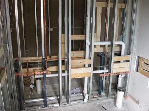 Exposed bathroom wall framing with metal studs, pipes, and wooden braces during renovation