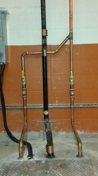 Three upright pipes against a wall, with a black center pipe and copper side pipes in a utility area