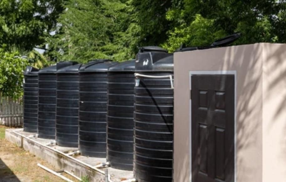 Row of large black water tanks beside a beige building in a sunny outdoor area