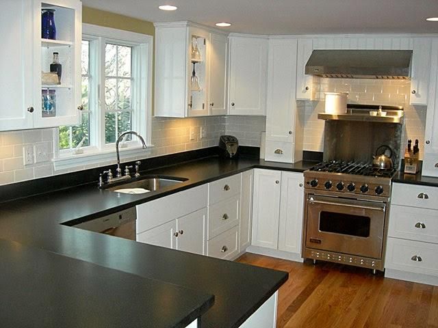 Modern kitchen with black countertops, white cabinets, stainless stove, and large window over the sink