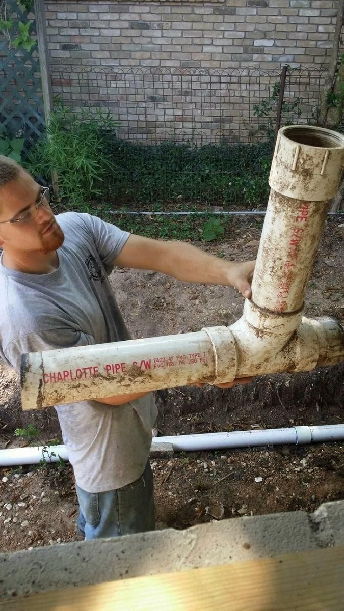 Worker installing large white pipes in a trench beside a brick wall