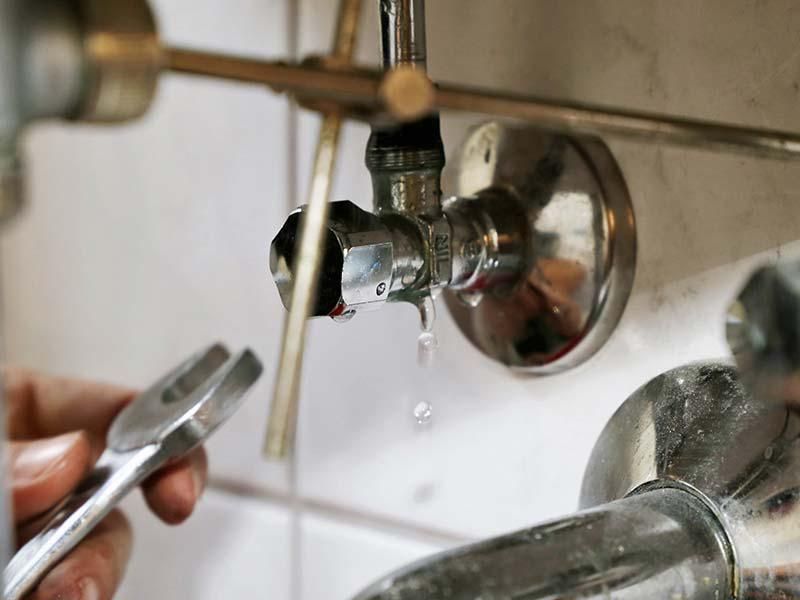 Hand turning off a leaky chrome faucet over a white sink in a tiled bathroom