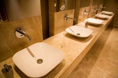 Row of white sink basins with wall-mounted faucets in a beige public restroom.