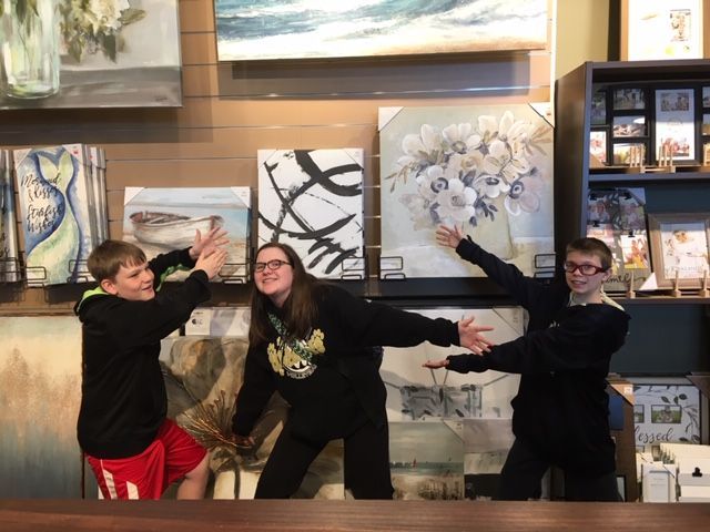 Three people posing with arms out in an art gallery, with framed paintings on the wall.