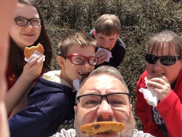 Five people outdoors smiling and eating cookies in bright sunlight