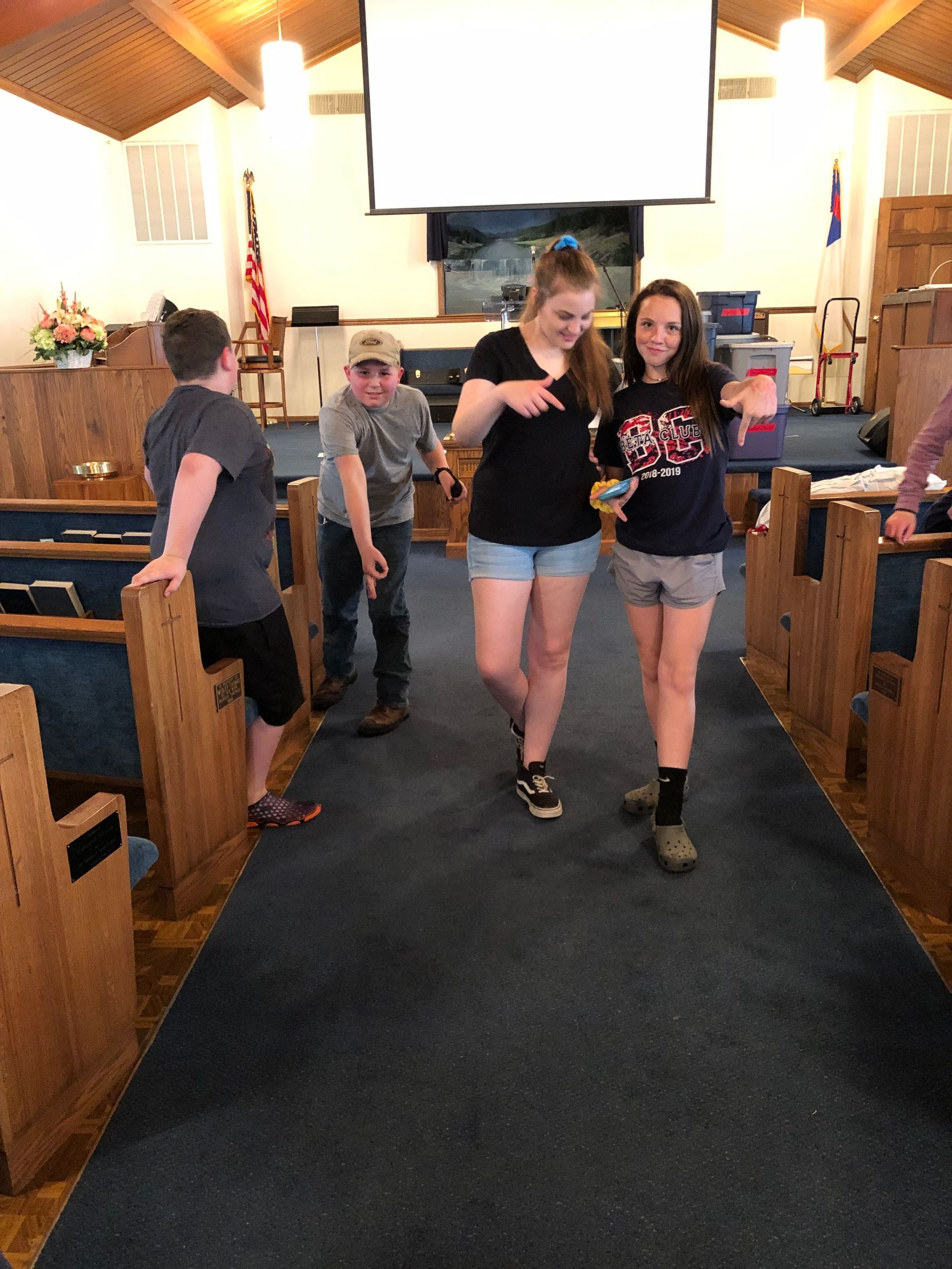 Two people walking down a church aisle toward the camera, with pews and a projection screen behind them.