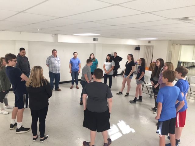 People standing in a circle in a bright room, appearing to take part in a group activity or discussion